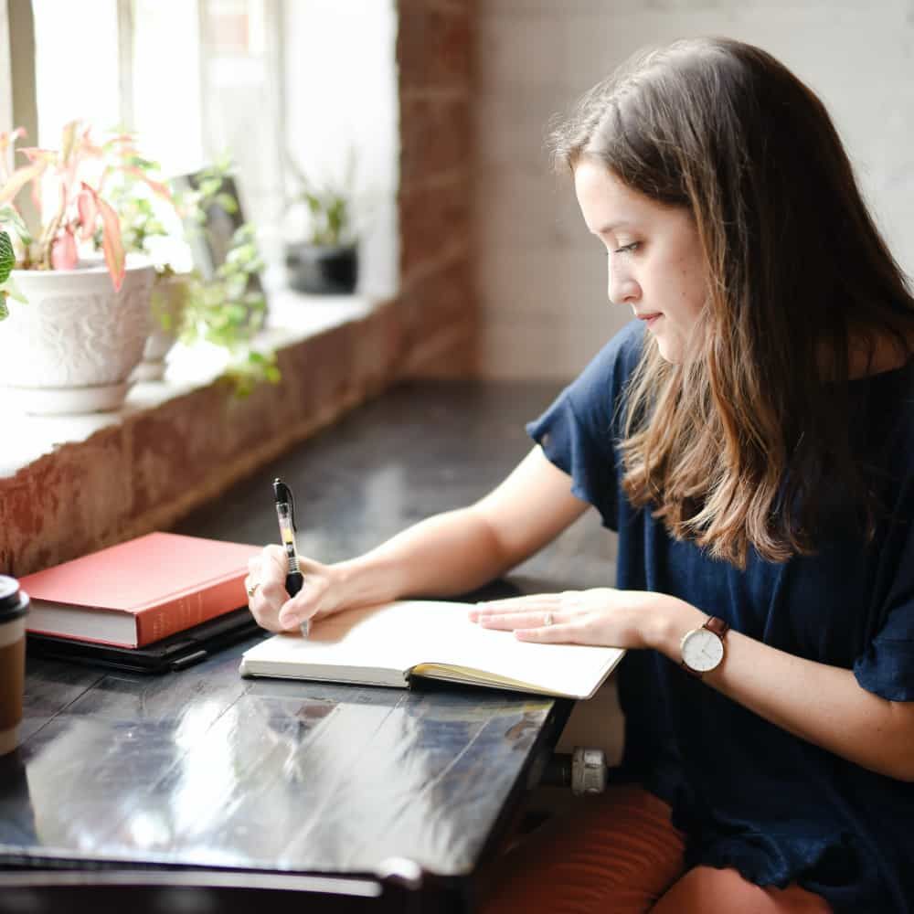 Mulher sentada em uma mesa escrevendo em um bloco de notas